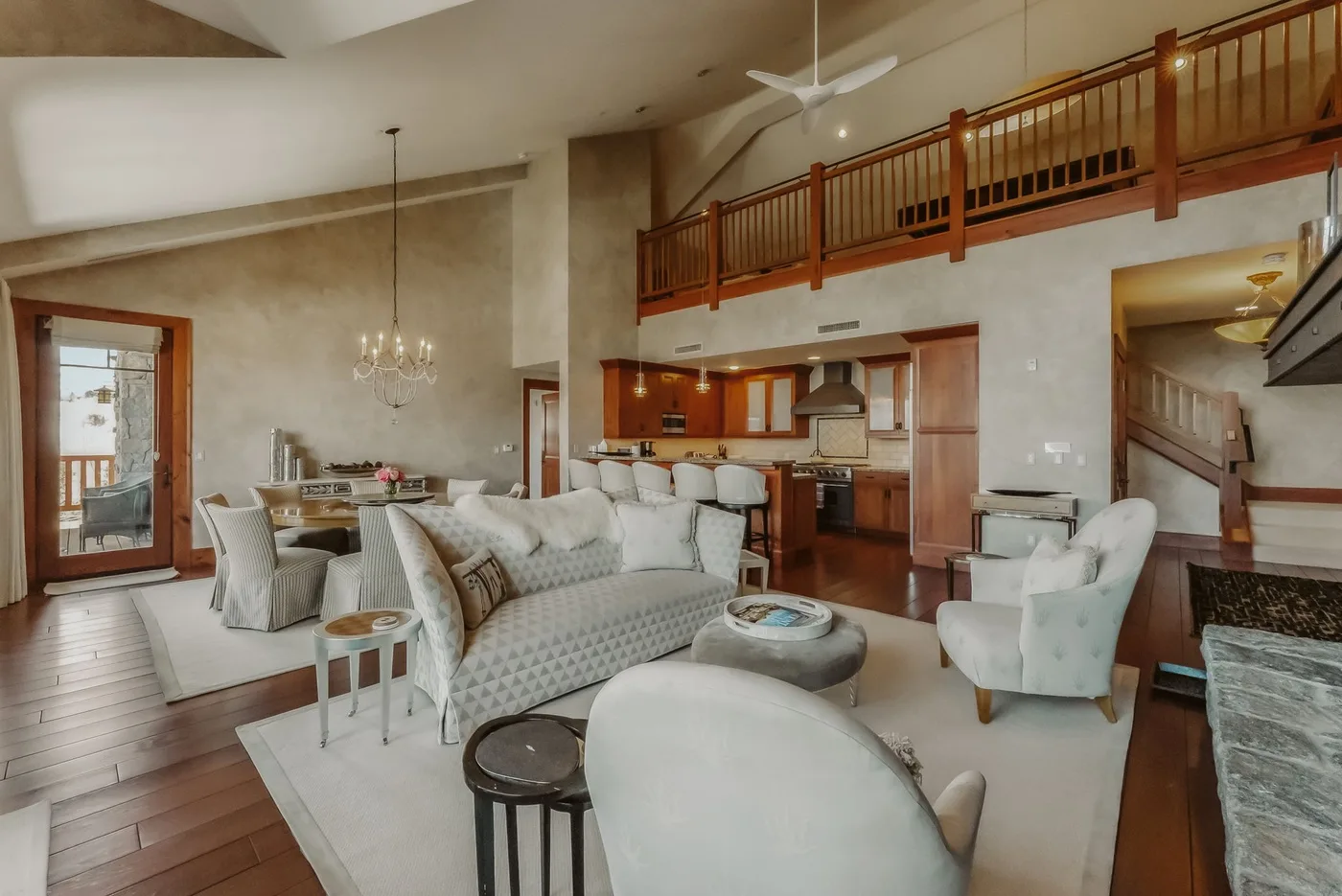 Una luminosa sala de estar diáfana con comedor y cocina bajo un balcón de madera.