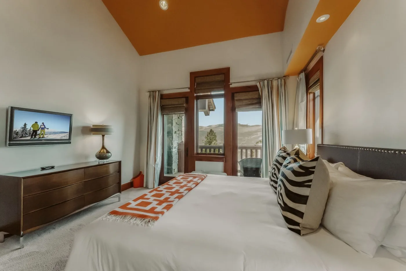 Un dormitorio con una cama grande, una alfombra estampada y ventanas con vistas al paisaje.