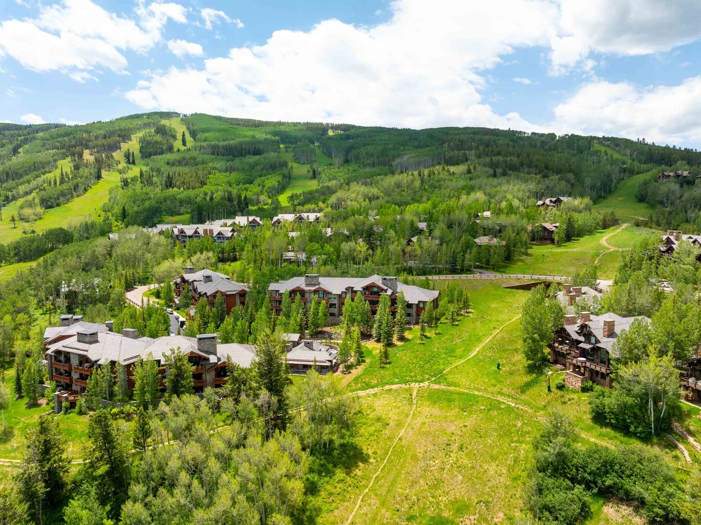 Un complejo turístico en una ladera está rodeado de bosque verde y praderas abiertas.