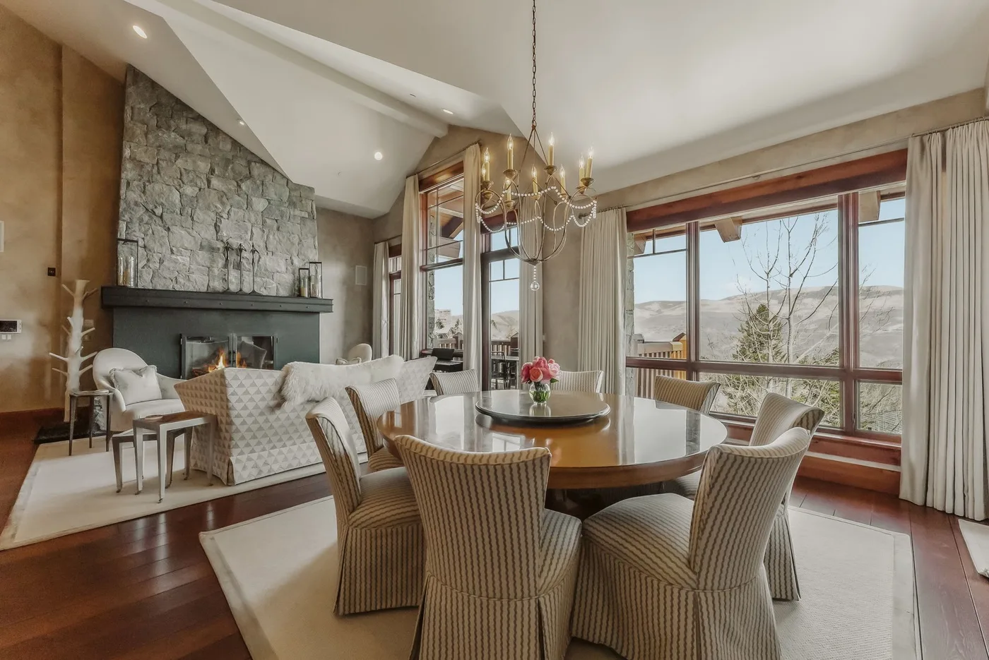 Comedor con asientos tejidos, grandes ventanales y una chimenea de piedra.