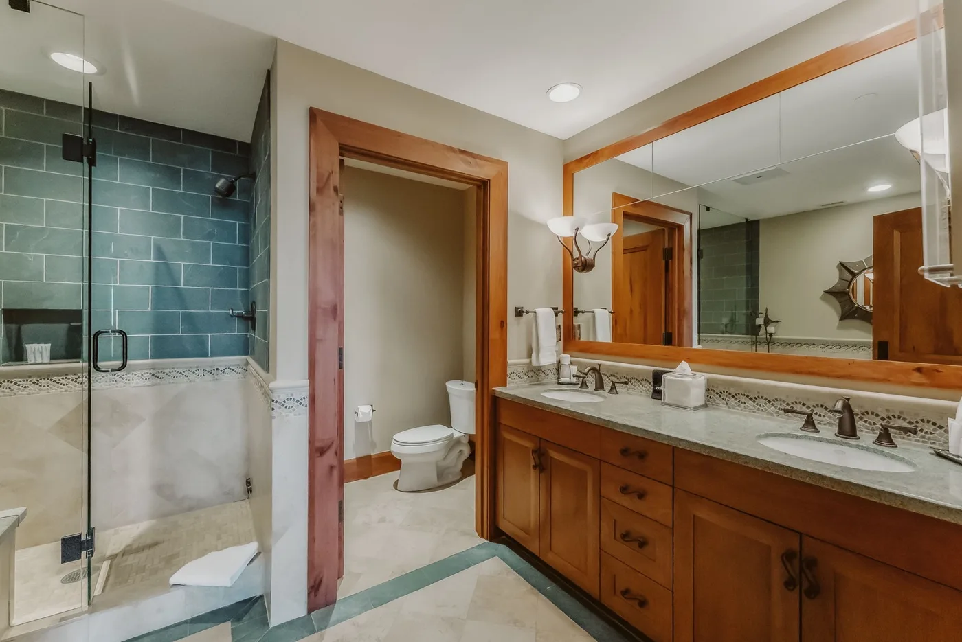 Un baño con ducha de vidrio, inodoro y un largo tocador de madera.