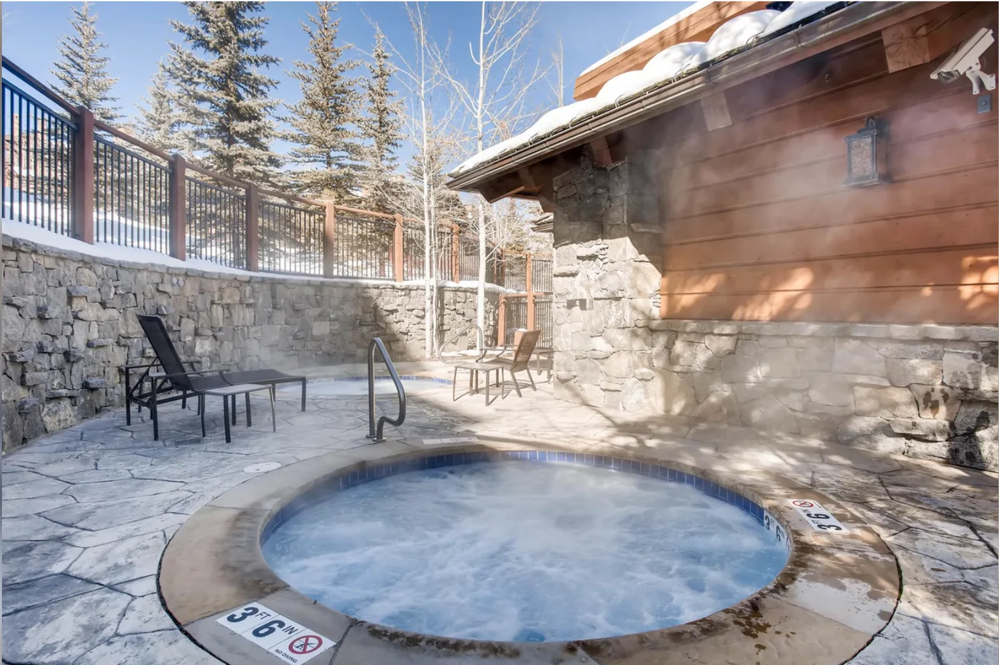 Una bañera de hidromasaje exterior está en un patio de piedra junto a un edificio de madera.