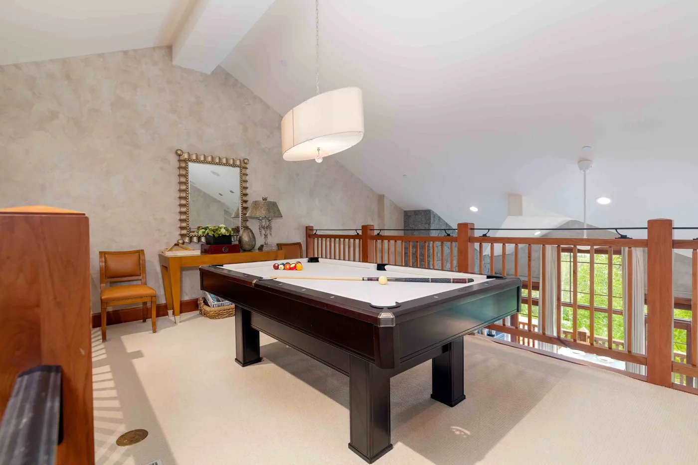 A game room with a billiards table beside a wooden railing.