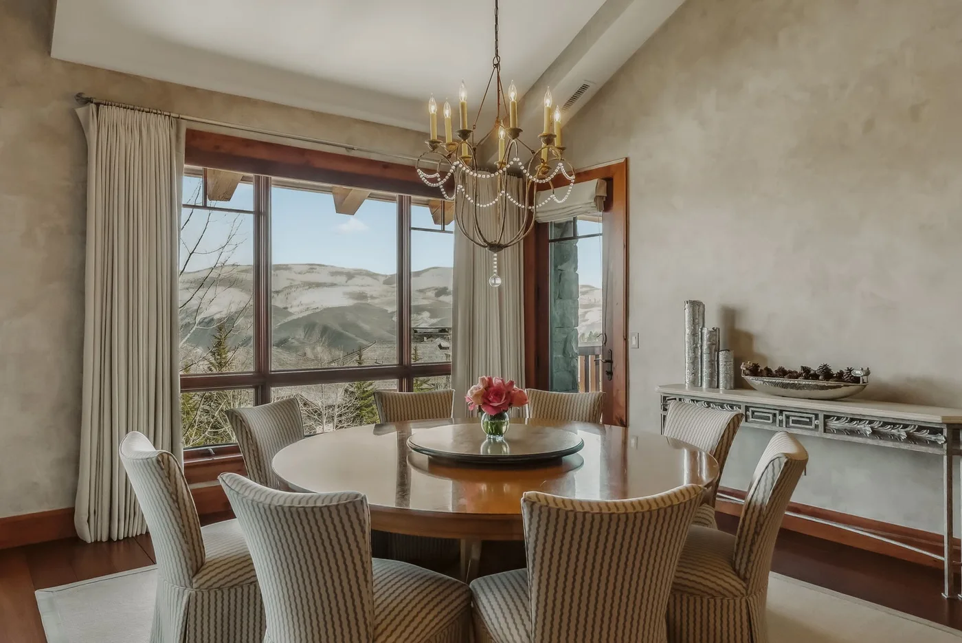 Un comedor con una mesa redonda y grandes ventanas con vistas a un paisaje montañoso.
