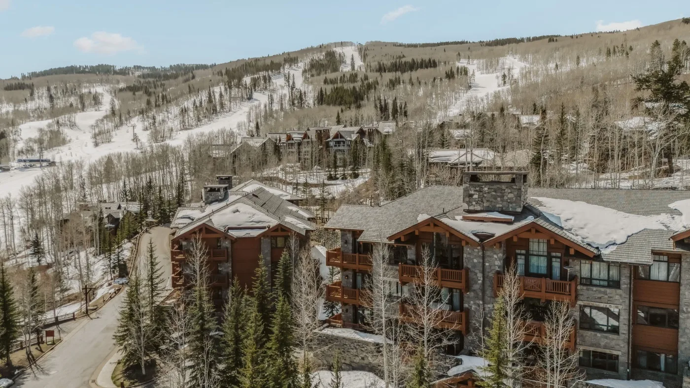Un edificio tipo lodge está entre árboles nevados, con pistas de esquí en la ladera del fondo.