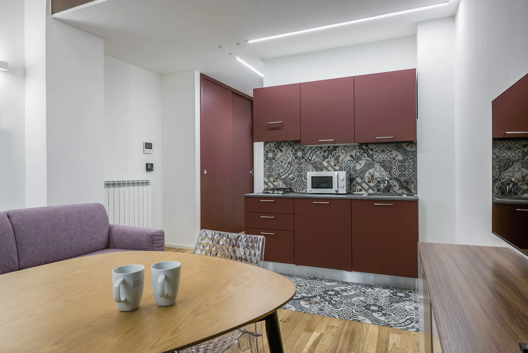 A modern kitchen and dining area with burgundy cabinets and a round table.