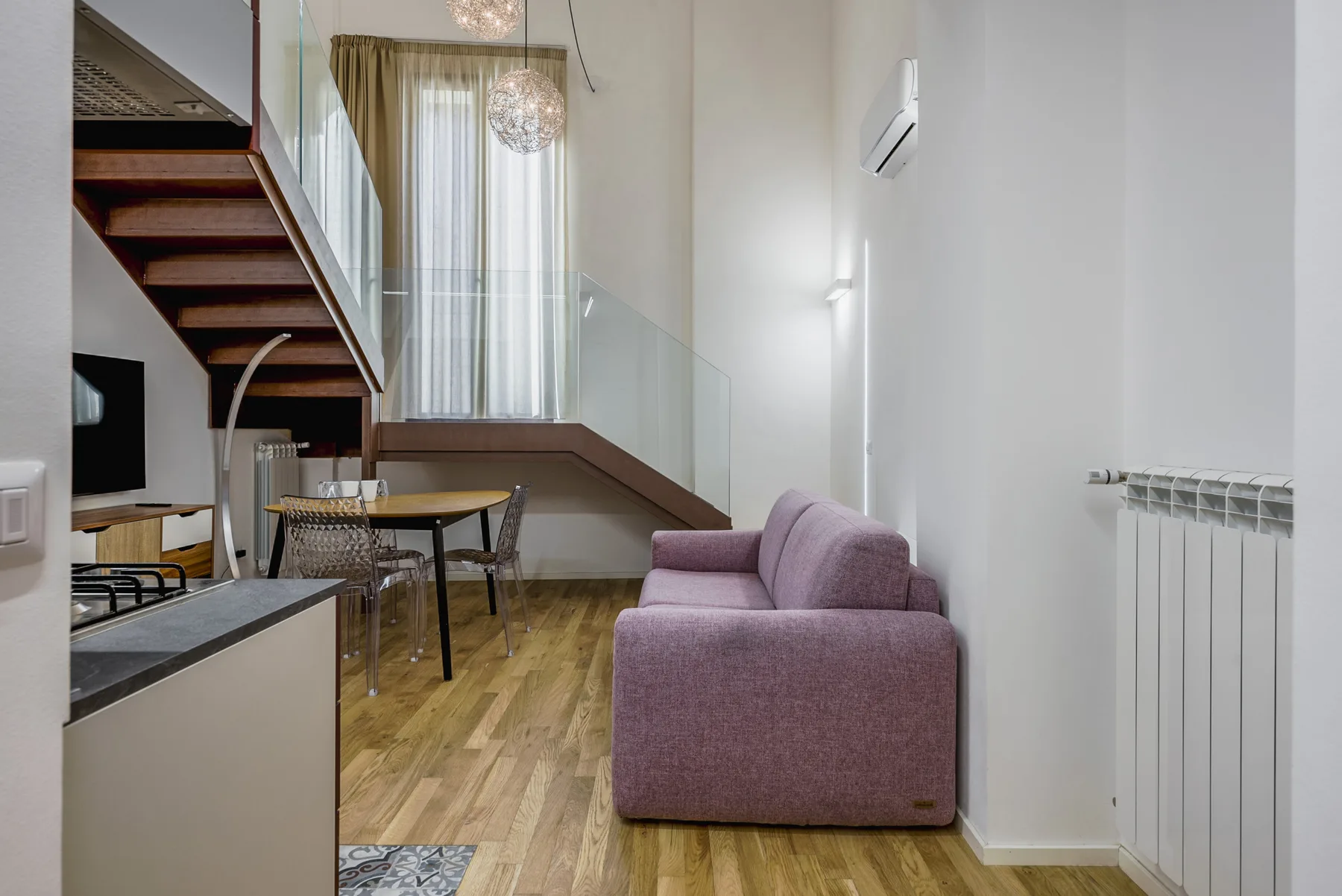 Una luminosa zona de estar y comedor tiene un sofá morado bajo una escalera.