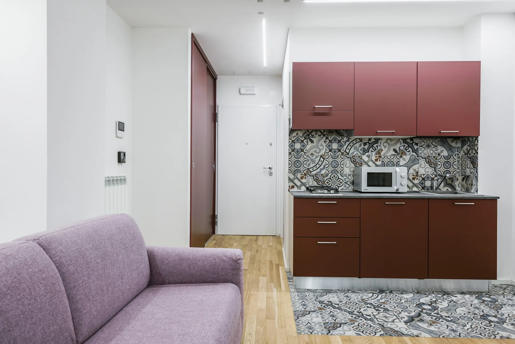 Una pequeña sala se abre a una cocina con azulejos estampados y gabinetes oscuros.
