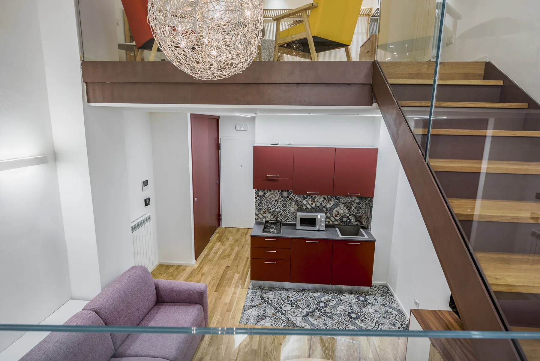 A compact kitchen beneath a staircase, with red cabinets and patterned tile.