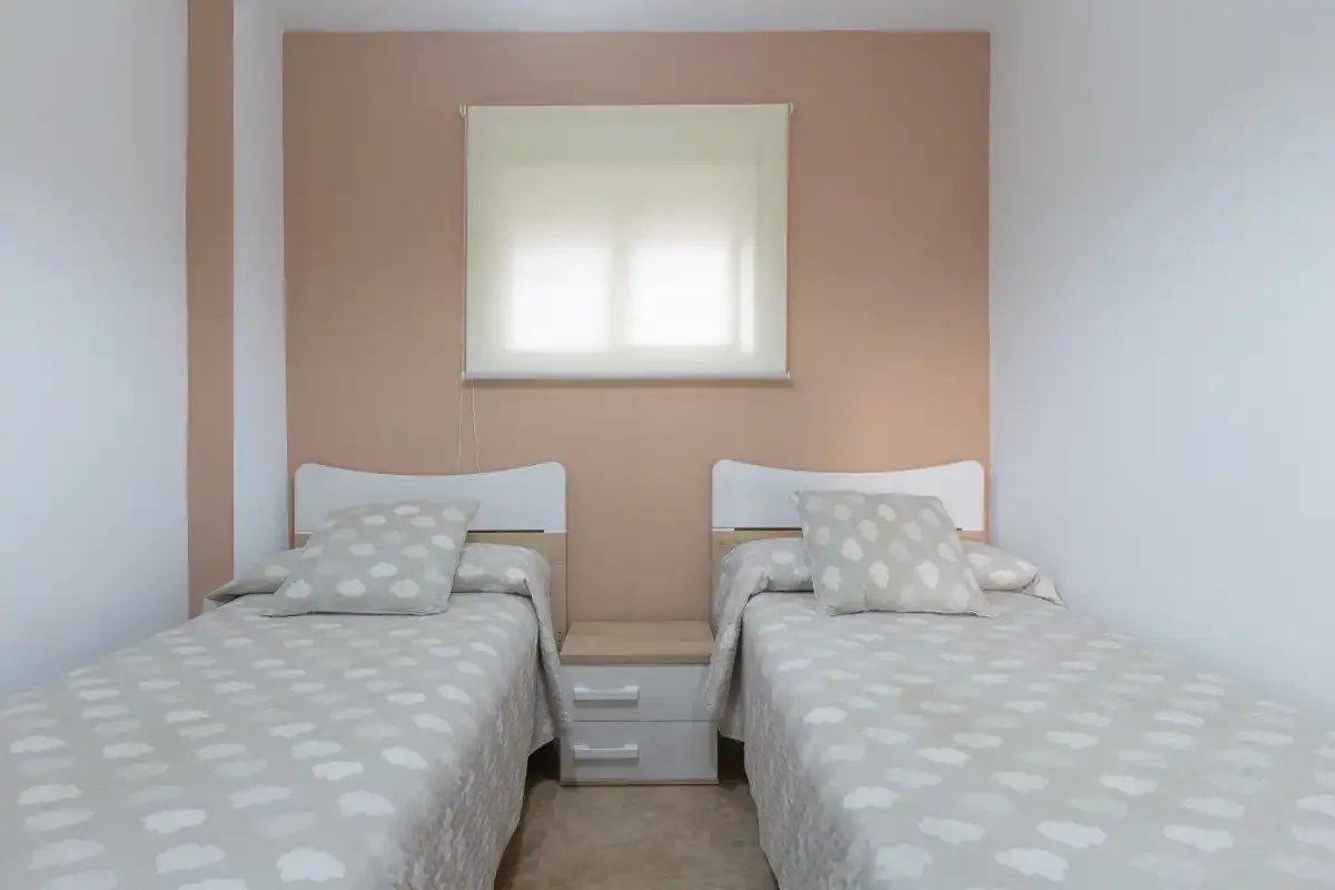 A twin bedroom with two beds beneath a small window.