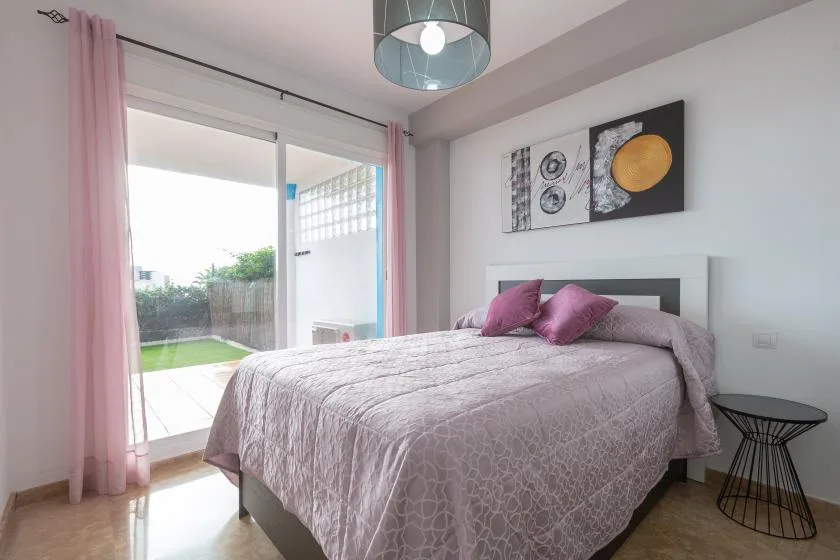 A bedroom with a bed, pink curtains, and a sliding glass door.