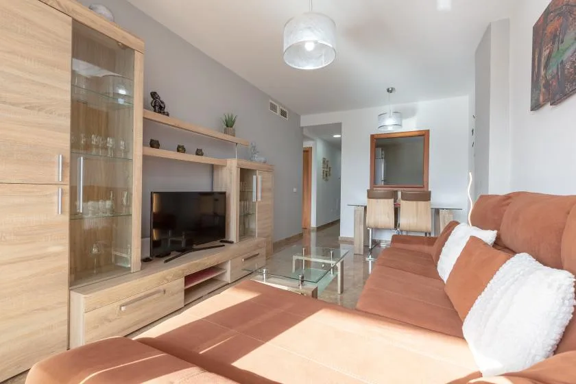 A bright living room with a television, glass coffee table, and seating.