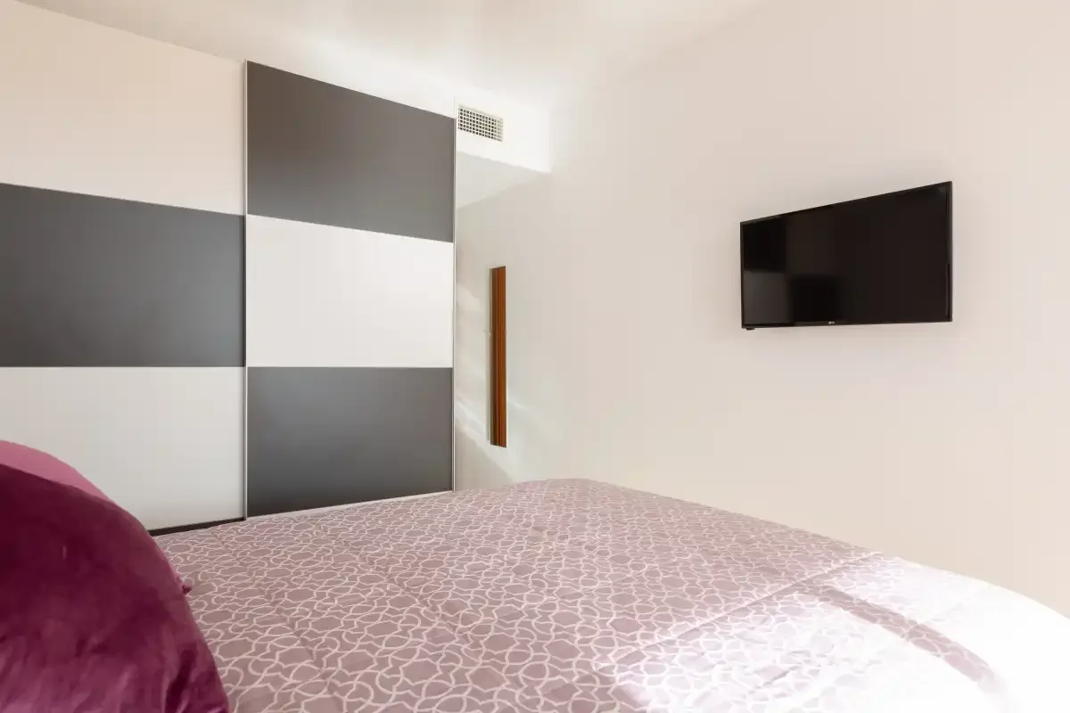 A bedroom with a patterned bedspread and a wall-mounted television.