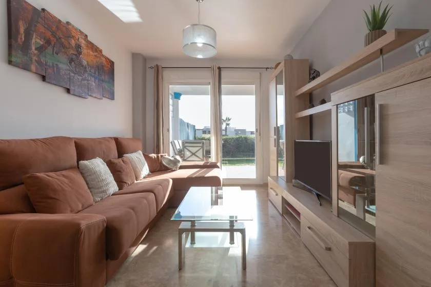A bright living room with seating, a glass coffee table, and large windows.