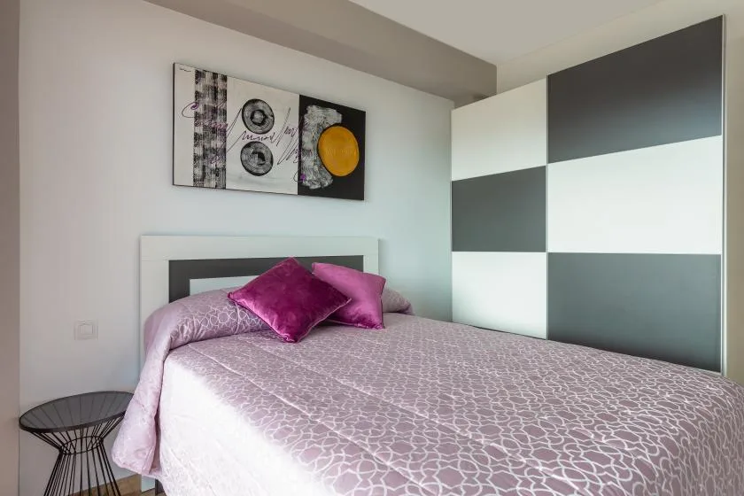 A bedroom with a bed dressed in a patterned cover and pink pillows.