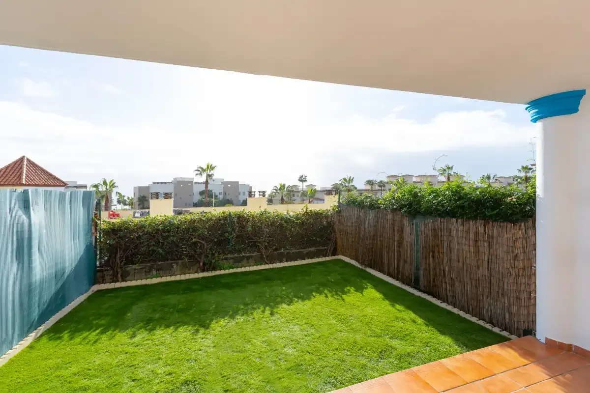 A grassy garden patio is bordered by hedges and a reed fence.