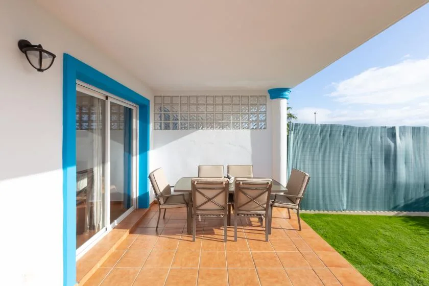 A covered patio with a dining table and seating overlooks a small lawn.