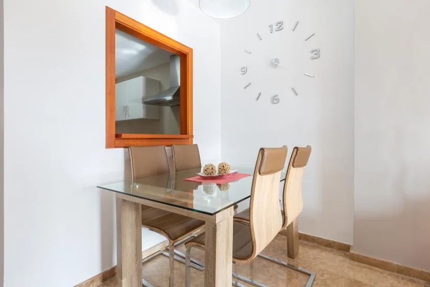 A dining area with a glass-top table and chairs beside a wall clock.