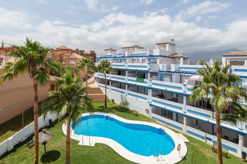A curved outdoor swimming pool sits beside a white-and-blue apartment building.