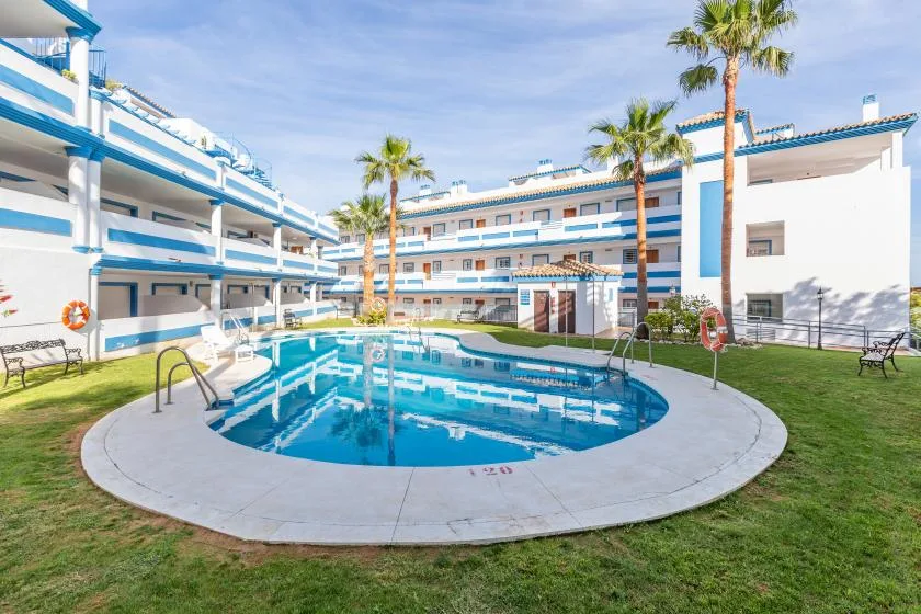 A swimming pool sits in a courtyard surrounded by white buildings and palm trees.