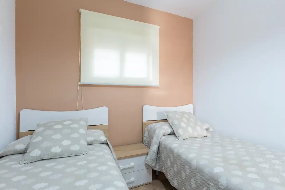 A bedroom with two single beds and a window above a bedside table.