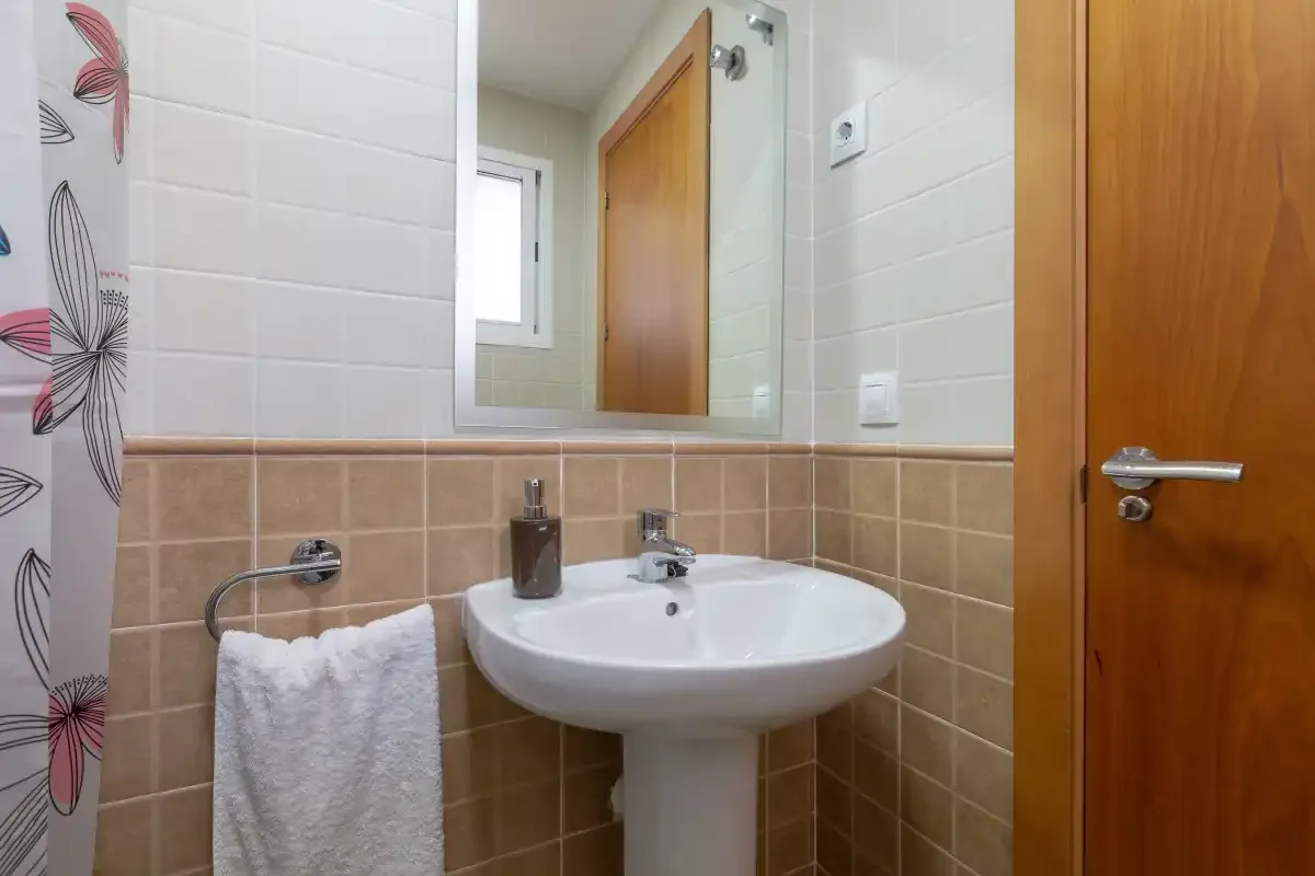 A tiled bathroom with a sink, mirror, and wooden door.