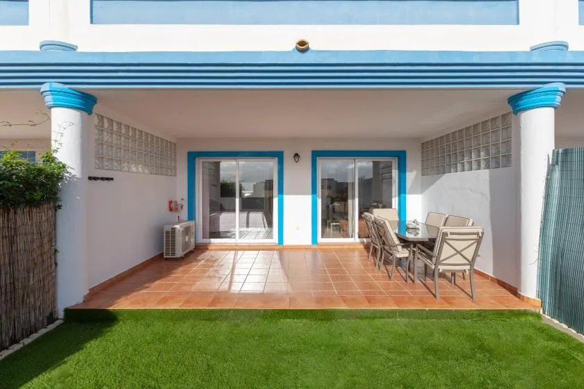 A covered patio with sliding glass doors, outdoor seating, and a lawn in front.