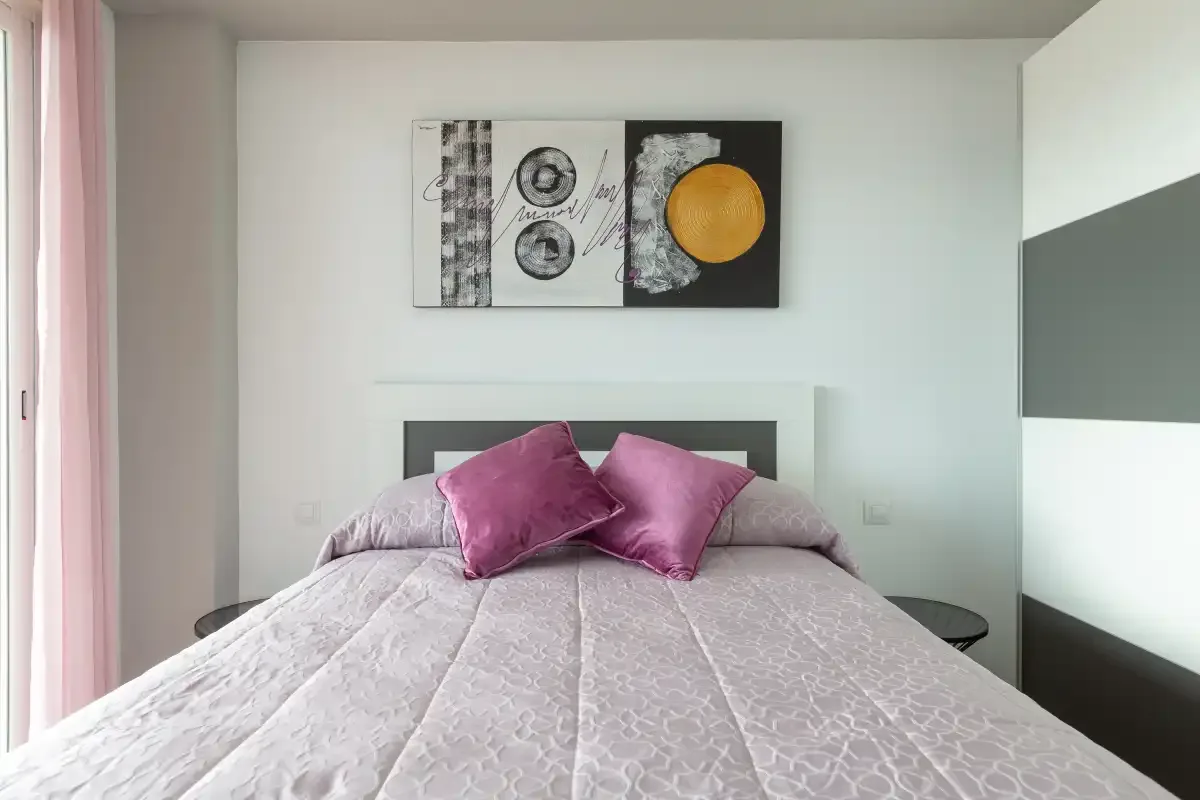 A bedroom with a bed dressed in pale bedding and purple pillows.