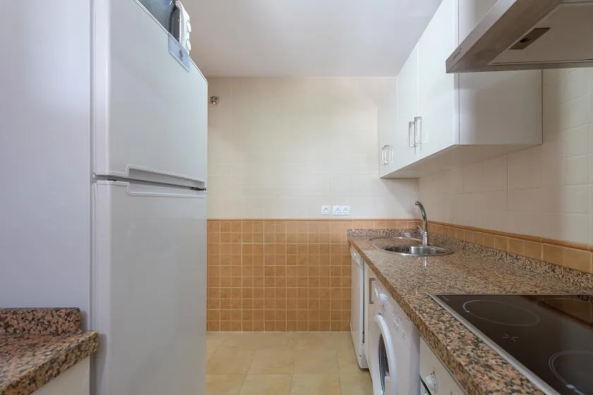 A compact kitchen with a refrigerator, countertop, sink, and cooktop.