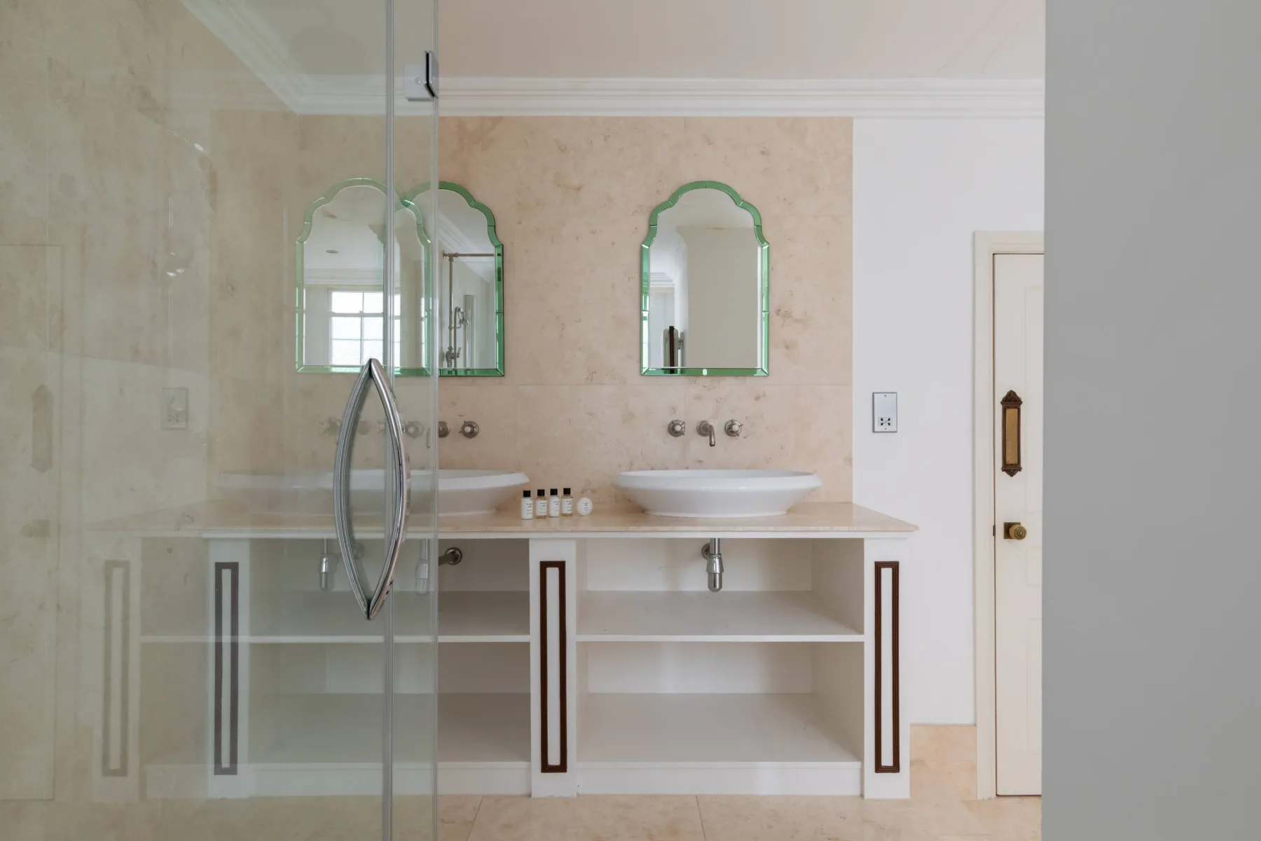 A bathroom with two sinks, green-framed mirrors, and a glass shower.