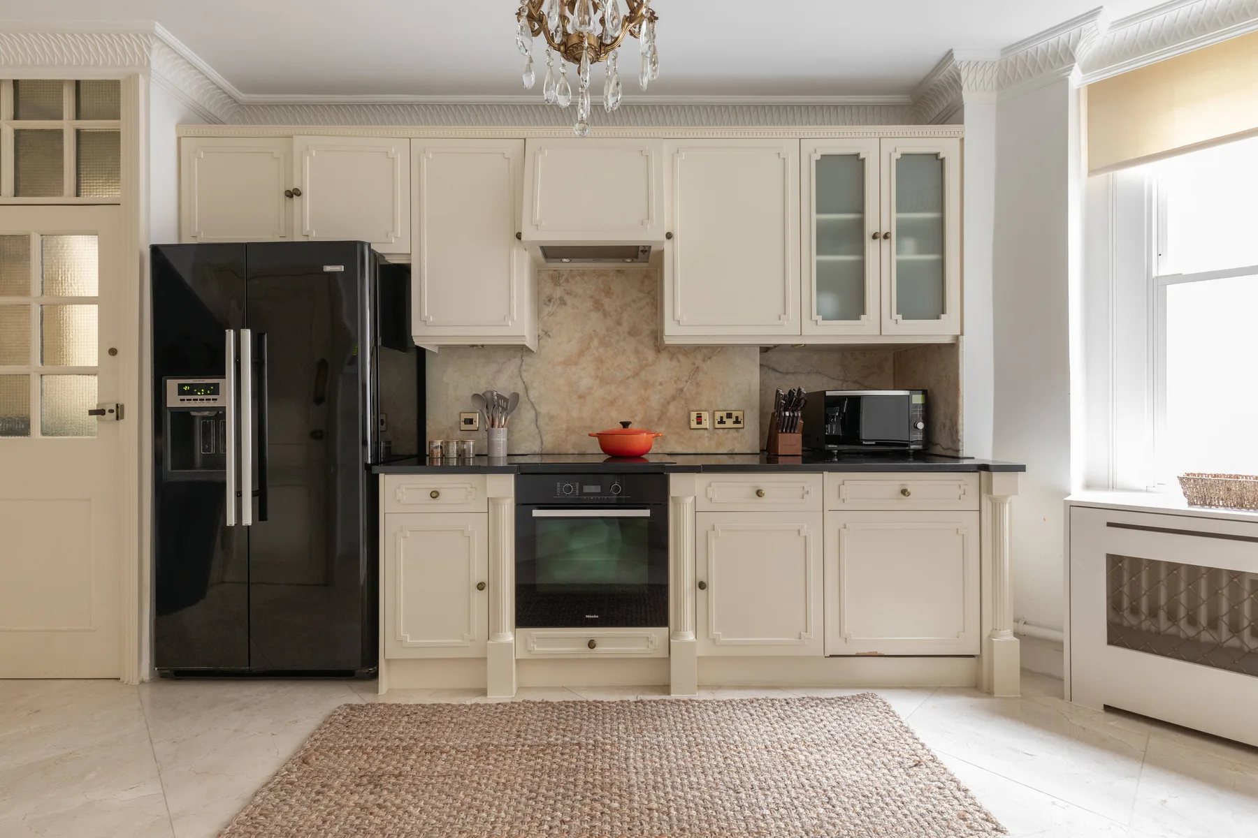 A bright kitchen with white cabinets, dark appliances, and a window.