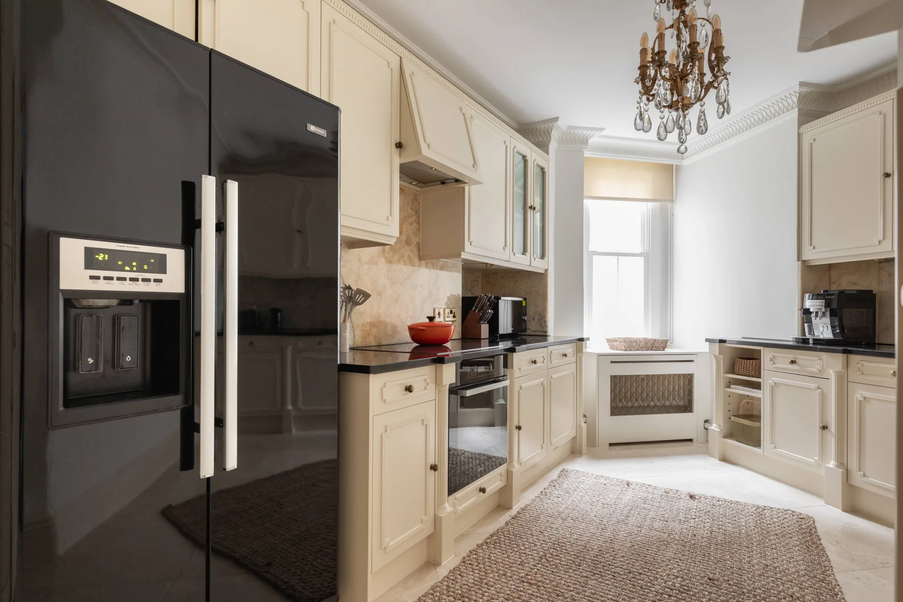 A bright kitchen with cream cabinetry, dark countertops, and a large black refrigerator.