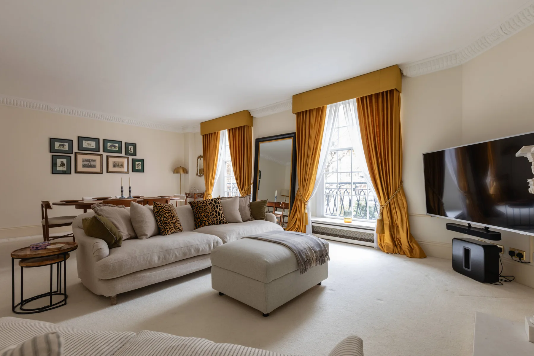 A bright living room with comfortable seating, tall windows, and golden curtains.