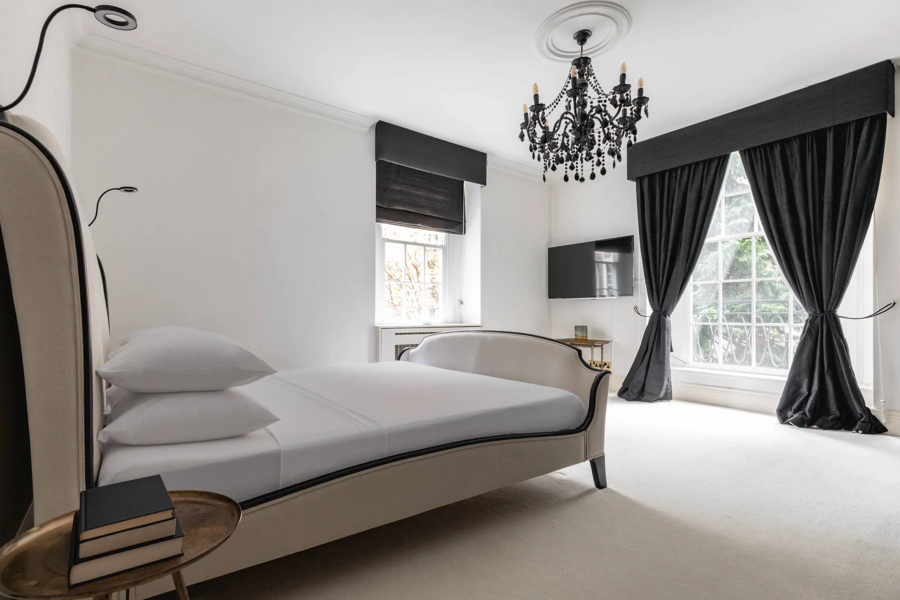 A bedroom with a large bed, dark curtains, and a chandelier.