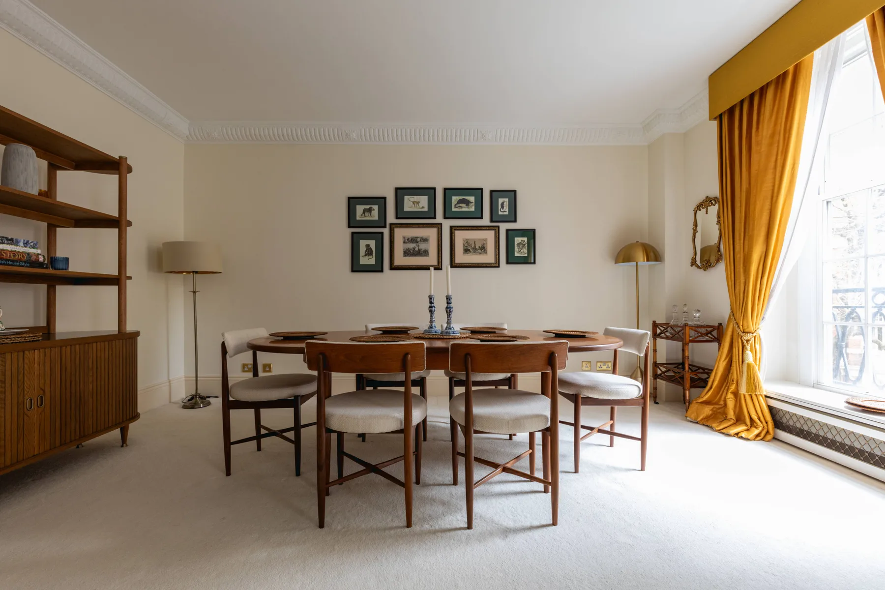 A dining room with a wooden table and chairs beside a large curtained window.
