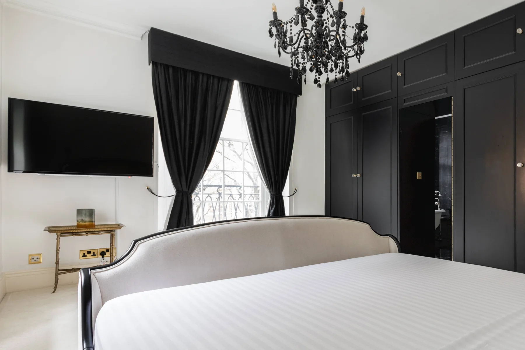 A bedroom with a large bed, black curtains, and dark built-in cabinets.