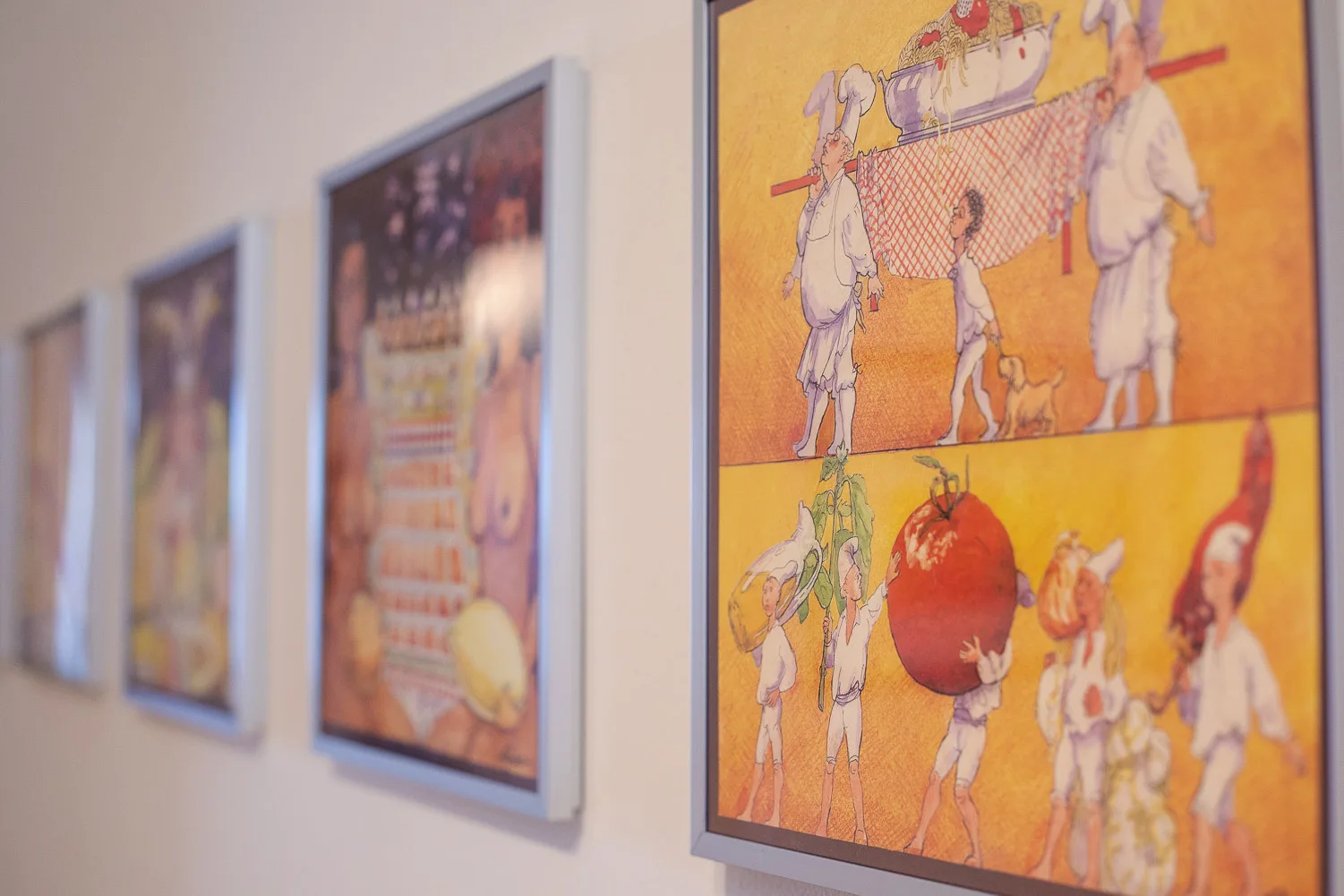 Una fila de ilustraciones coloridas enmarcadas cuelga de una pared clara.