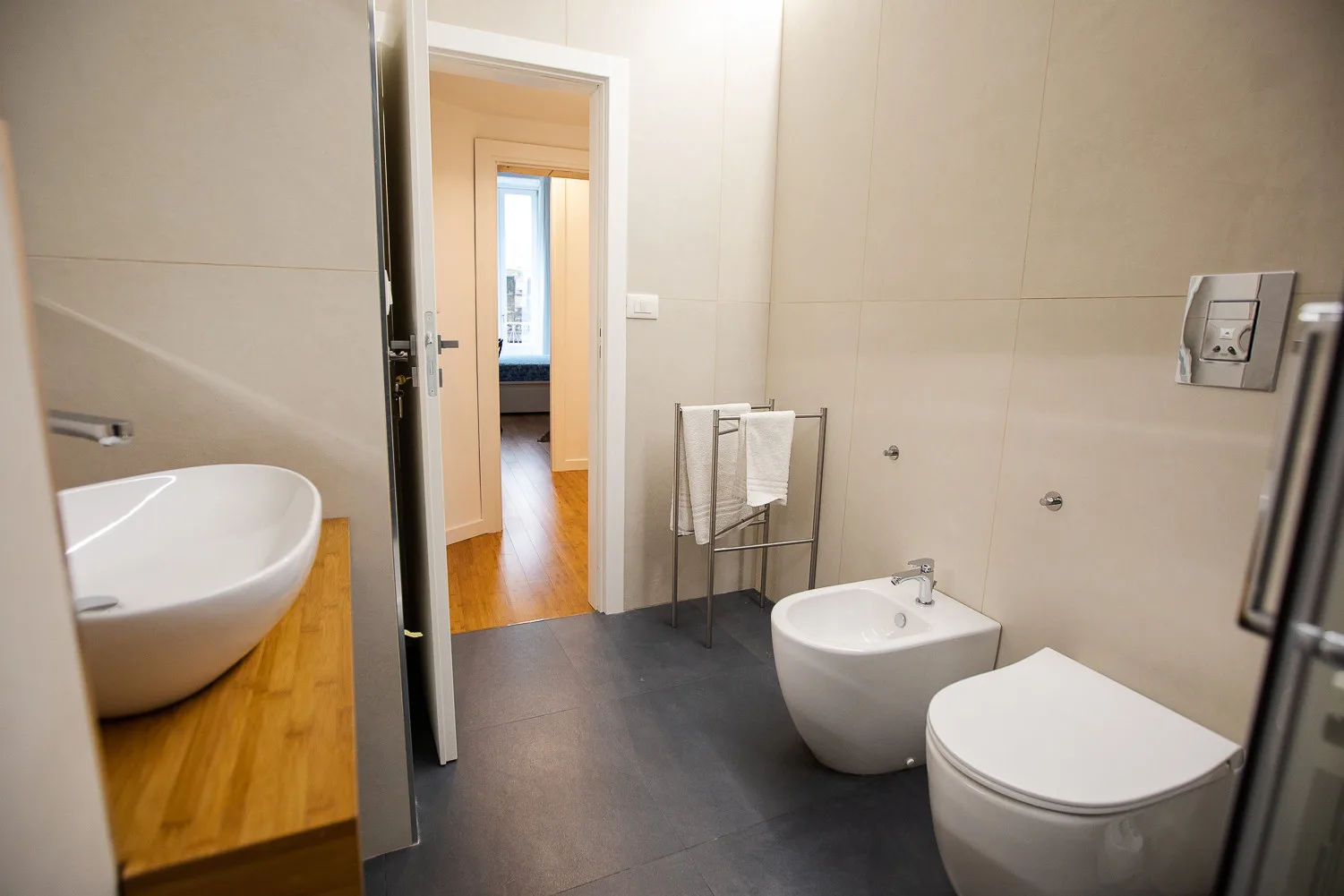 Un baño con azulejos, lavabo, inodoro y bidé junto a una puerta abierta.