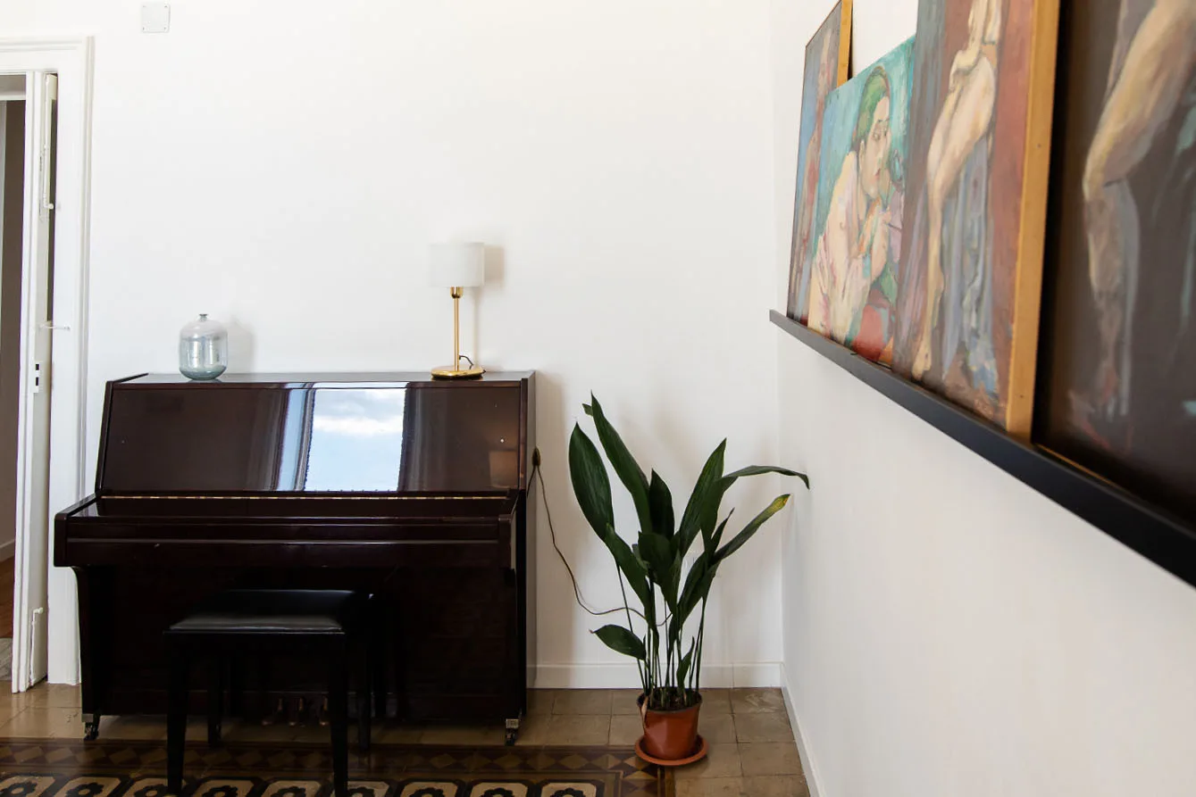 Un piano vertical, una planta en maceta y cuadros decoran una habitación luminosa.