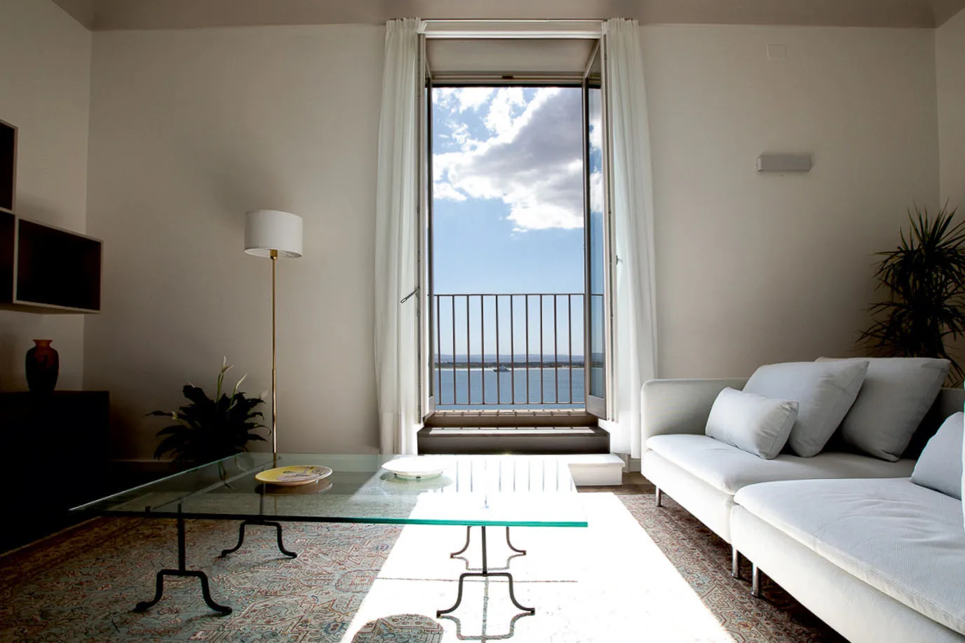 Una sala luminosa con asientos blancos junto a una ventana alta con vistas al mar.