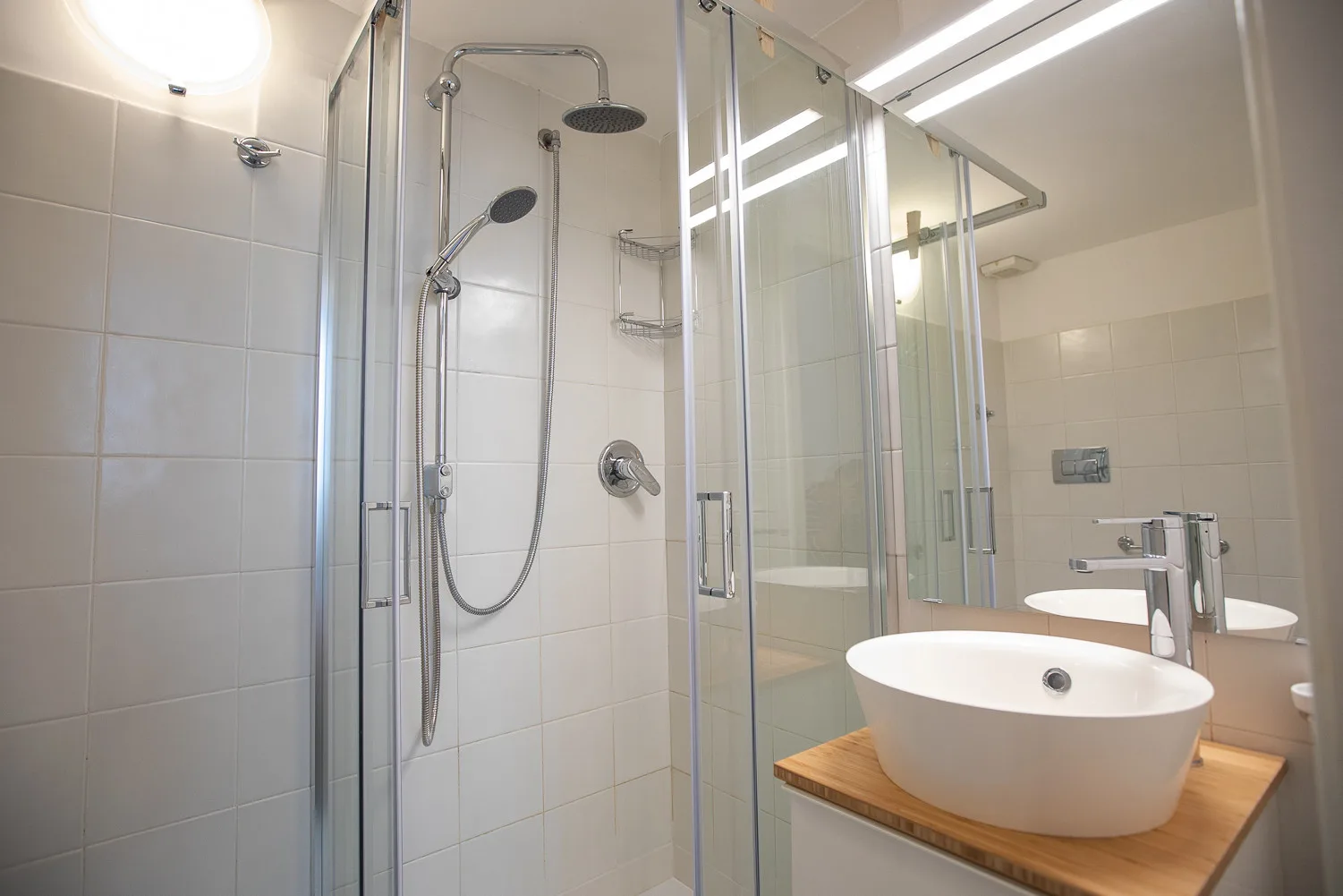 Un baño alicatado con ducha de vidrio y un lavabo blanco sobre una encimera de madera.