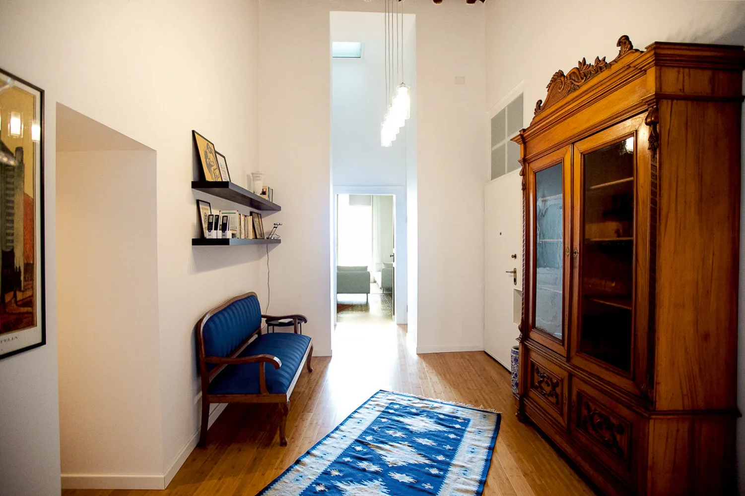 Un pasillo estrecho con un banco azul, estantes decorativos y un gran armario de madera.