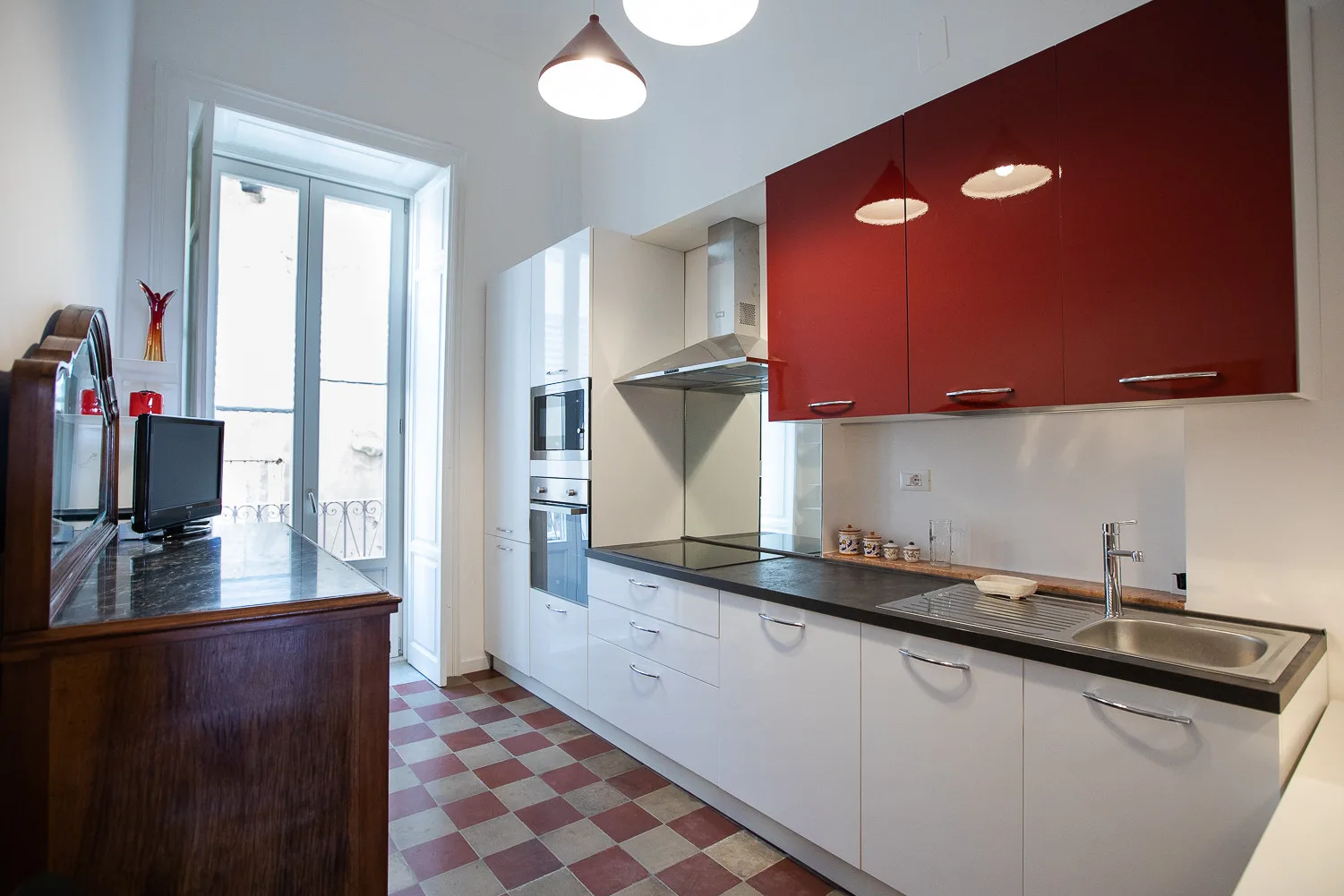 Una cocina moderna con armarios blancos, alacenas rojas y una encimera oscura.