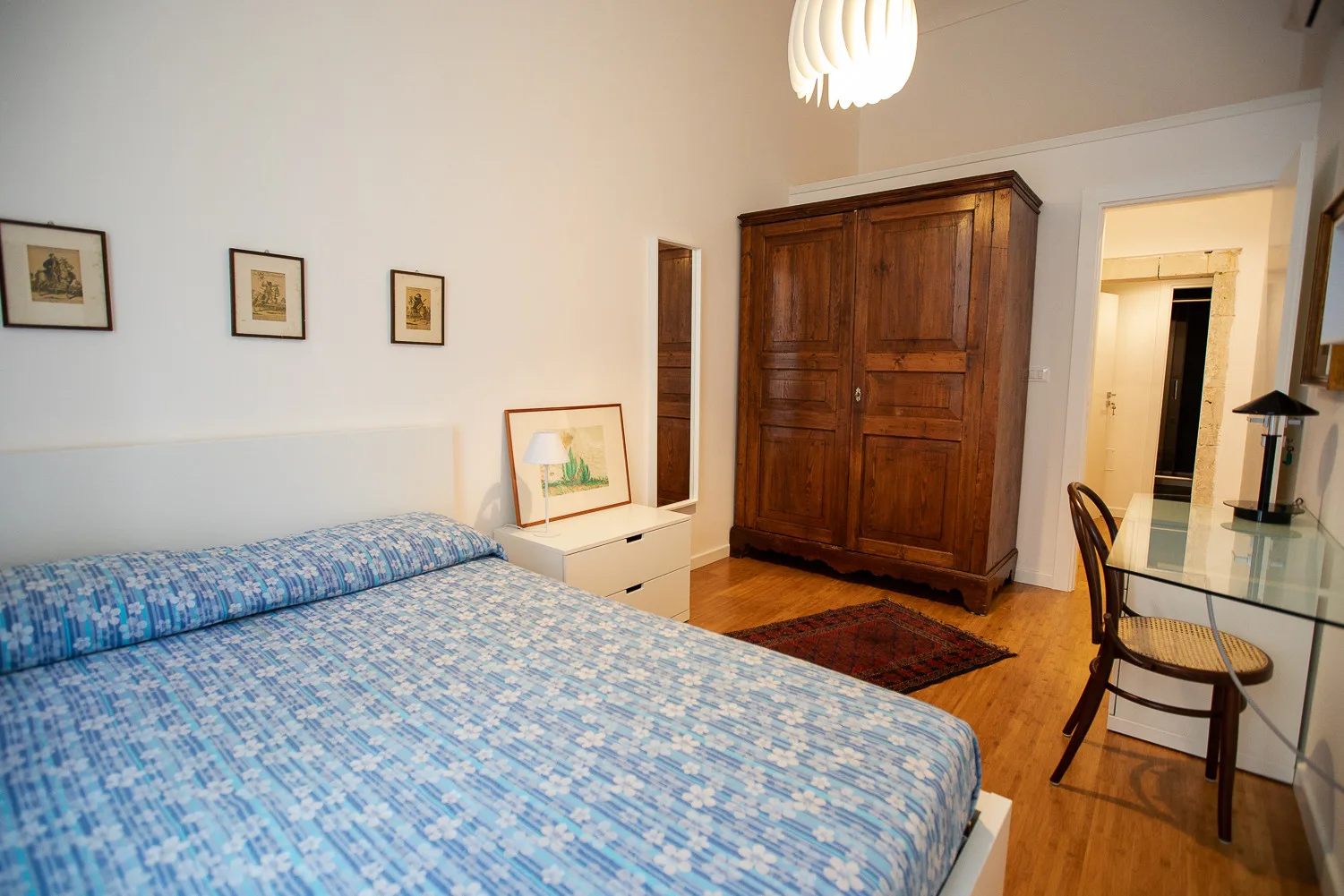 Un dormitorio con una cama, un armario de madera y un escritorio pequeño junto a la puerta.