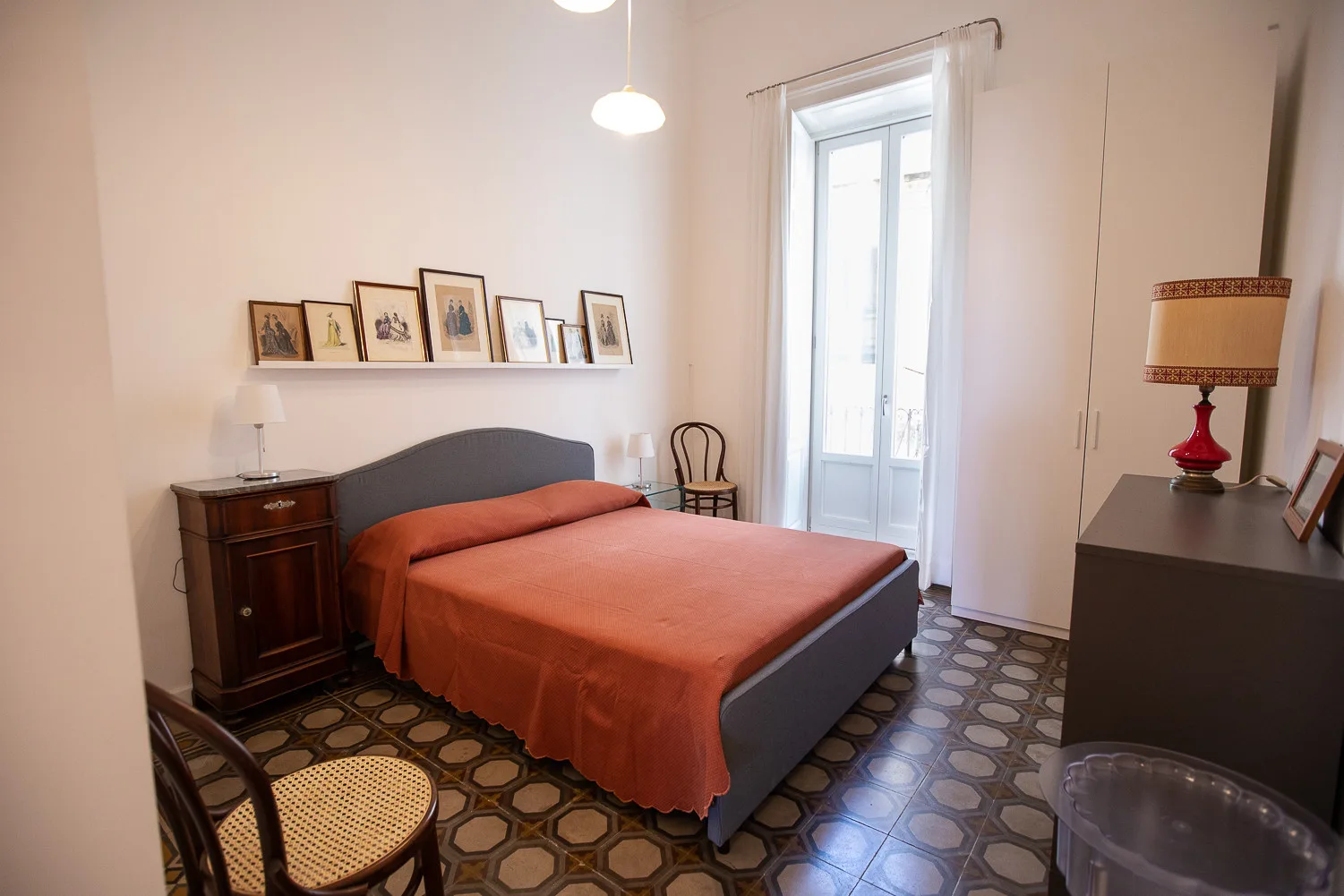 Un dormitorio con una cama, cuadros enmarcados y una ventana alta.