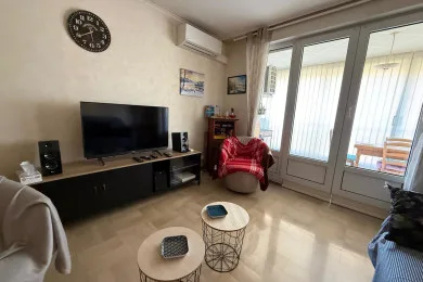 Una sala de estar con televisor, asientos y puertas de vidrio que dan a un balcón.