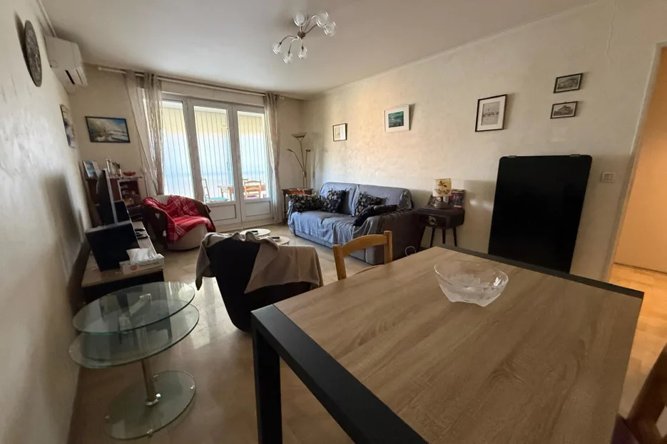 Una sala de estar con una mesa de comedor en primer plano y asientos junto a las ventanas.