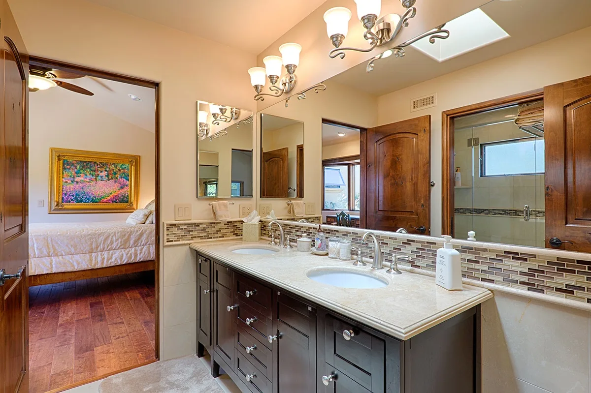 A bathroom vanity with a large mirror and a bedroom visible through the doorway.