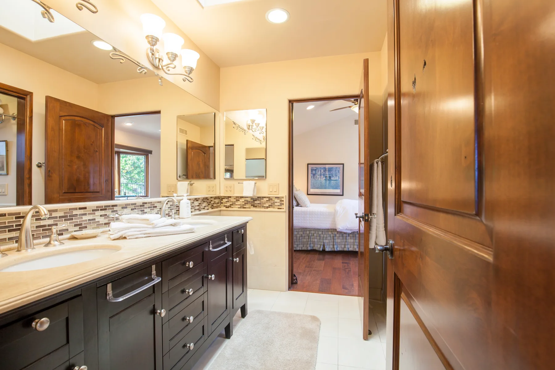 A bathroom vanity with sinks and mirrors opens onto a bedroom.