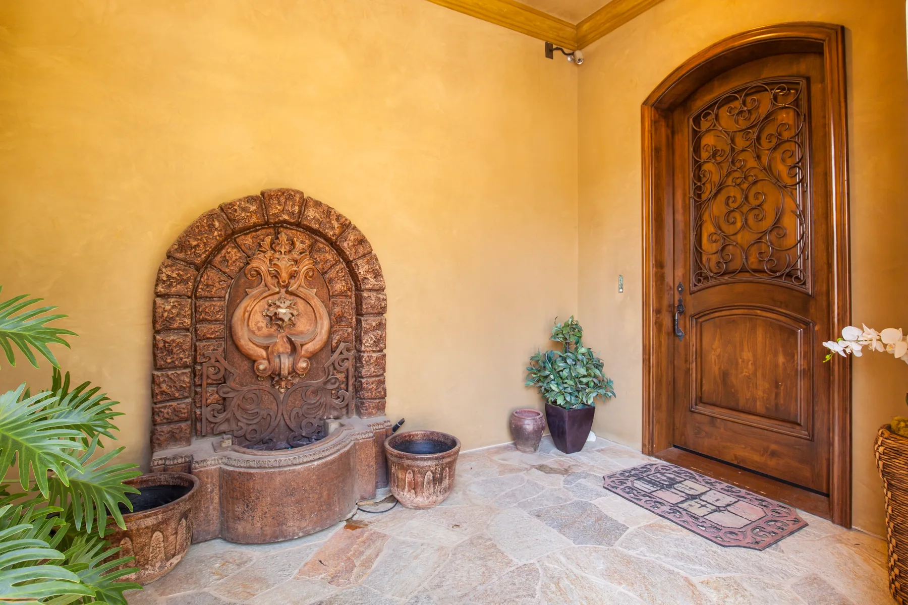 A warm-toned entryway with a carved wooden door and a decorative stone fountain.